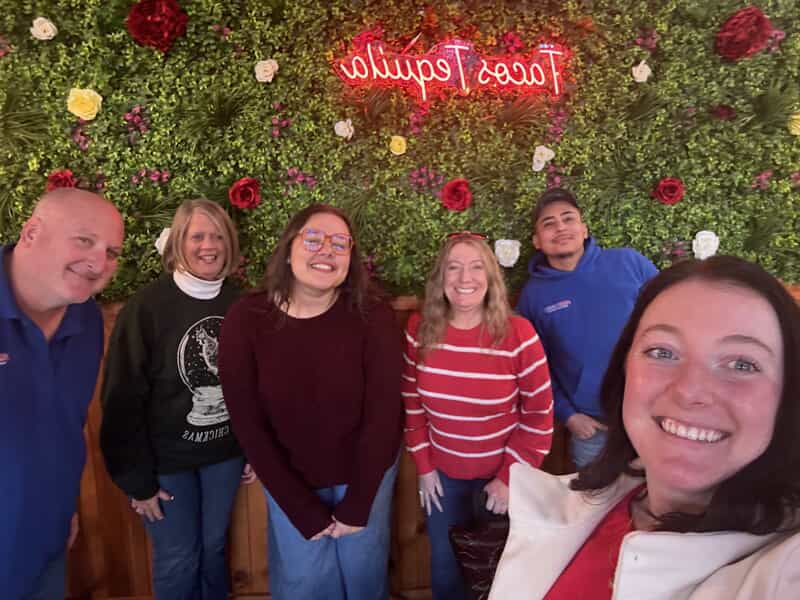 An image of a group of people taking a selfie under a neon Tacos Tequila sign.